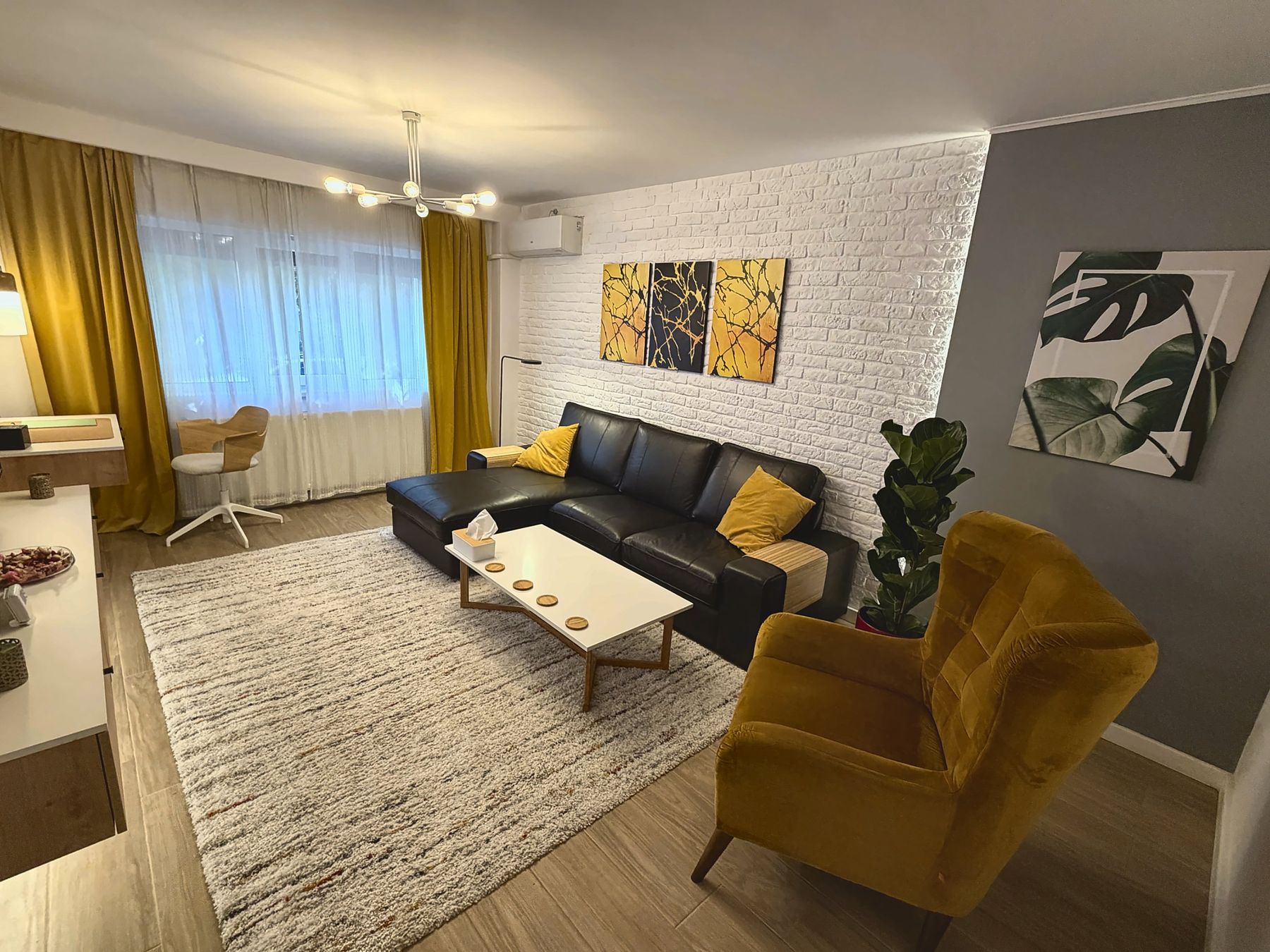Living-ul apartamentului, cu canapea, fotoliu galben și perete de cărămidă albă